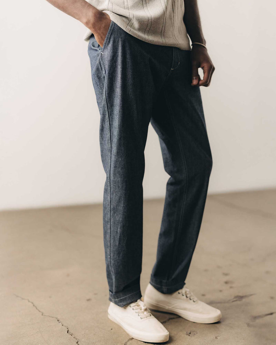 Person wearing dark blue jeans and white sneakers on a plain background