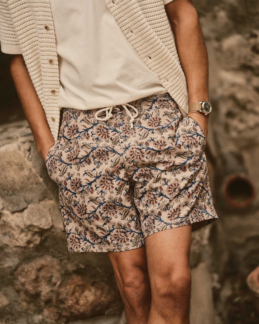 Person wearing floral shorts and a beige cardigan against a stone wall.