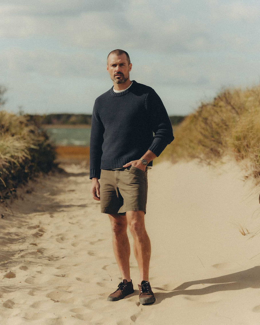Man standing on a sandy path with grass and water in the background
