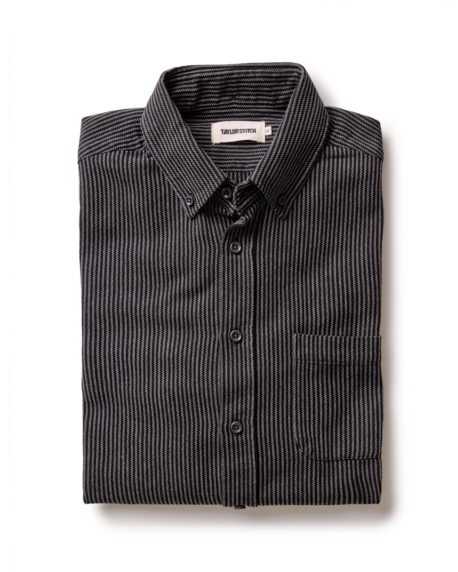 The Jack in Roped Black Indigo by Taylor Stitch, folded flat lay showing roped indigo stripe texture, button-down collar, and chest pocket with Taylor Stitch label