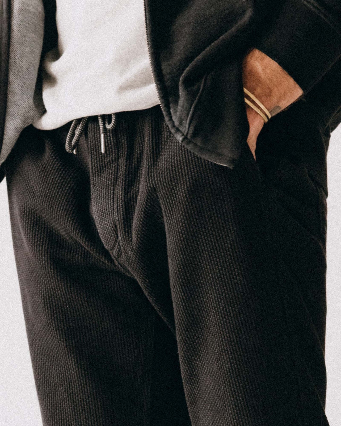 Person wearing dark textured pants with a neutral background