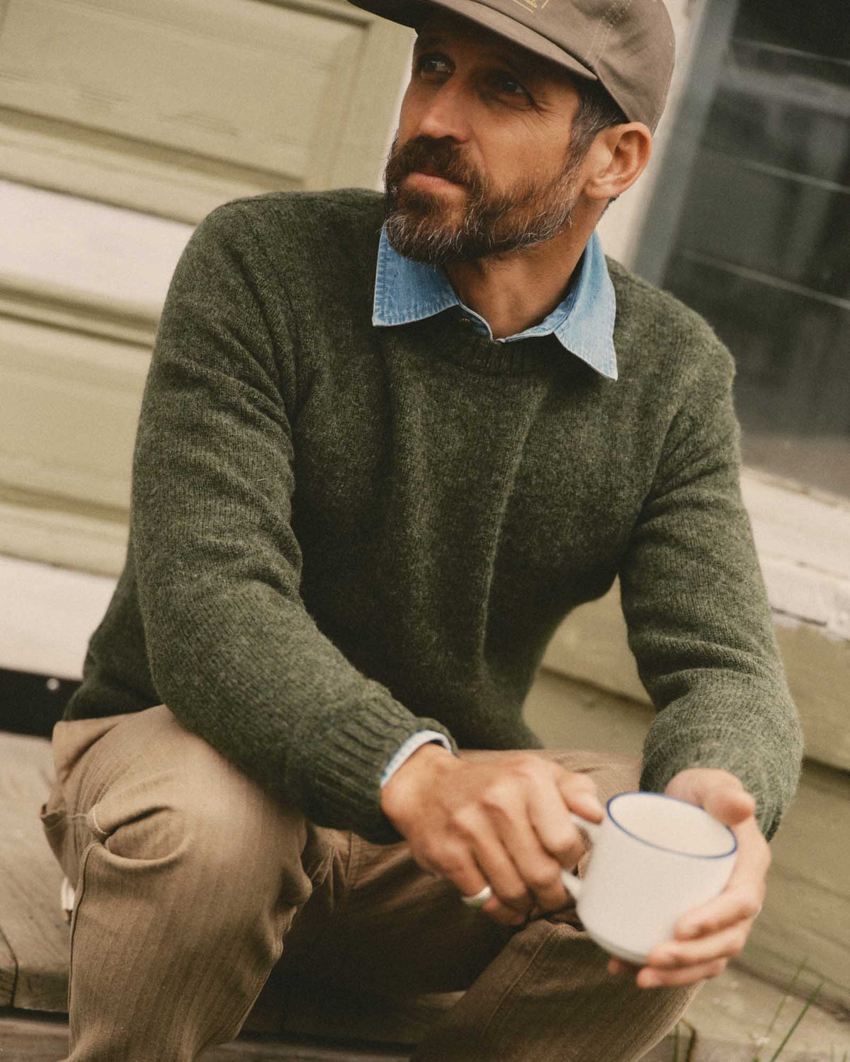 Model wearing the spruce green Eastmoor wool sweater over a blue collared shirt, seated outdoors.
