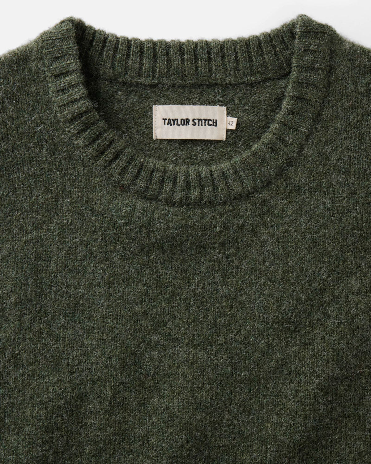 Close-up of the Eastmoor sweater’s ribbed crewneck, spruce green wool knit, and Taylor Stitch label.
