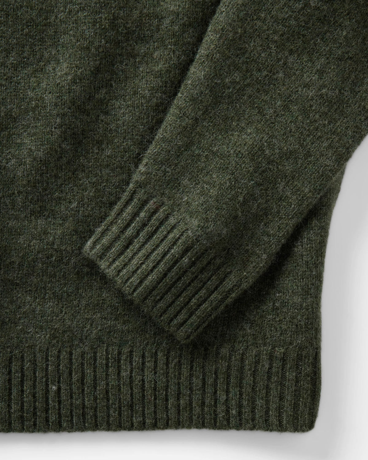 Close-up of the Eastmoor sweater’s spruce green wool texture, ribbed sleeve cuff, and ribbed hem.
