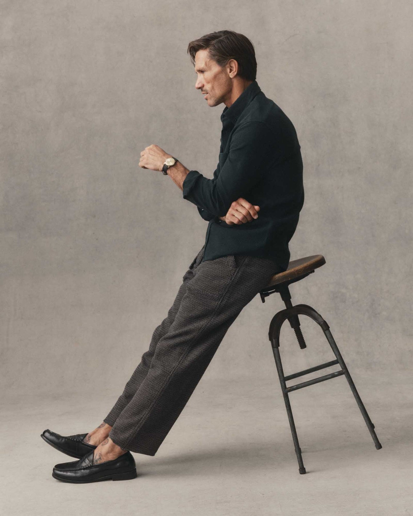 Male model wearing the Taylor Stitch Jack Shirt in Forest Waffle, seated side profile styled with dark trousers and black loafers against a neutral grey background