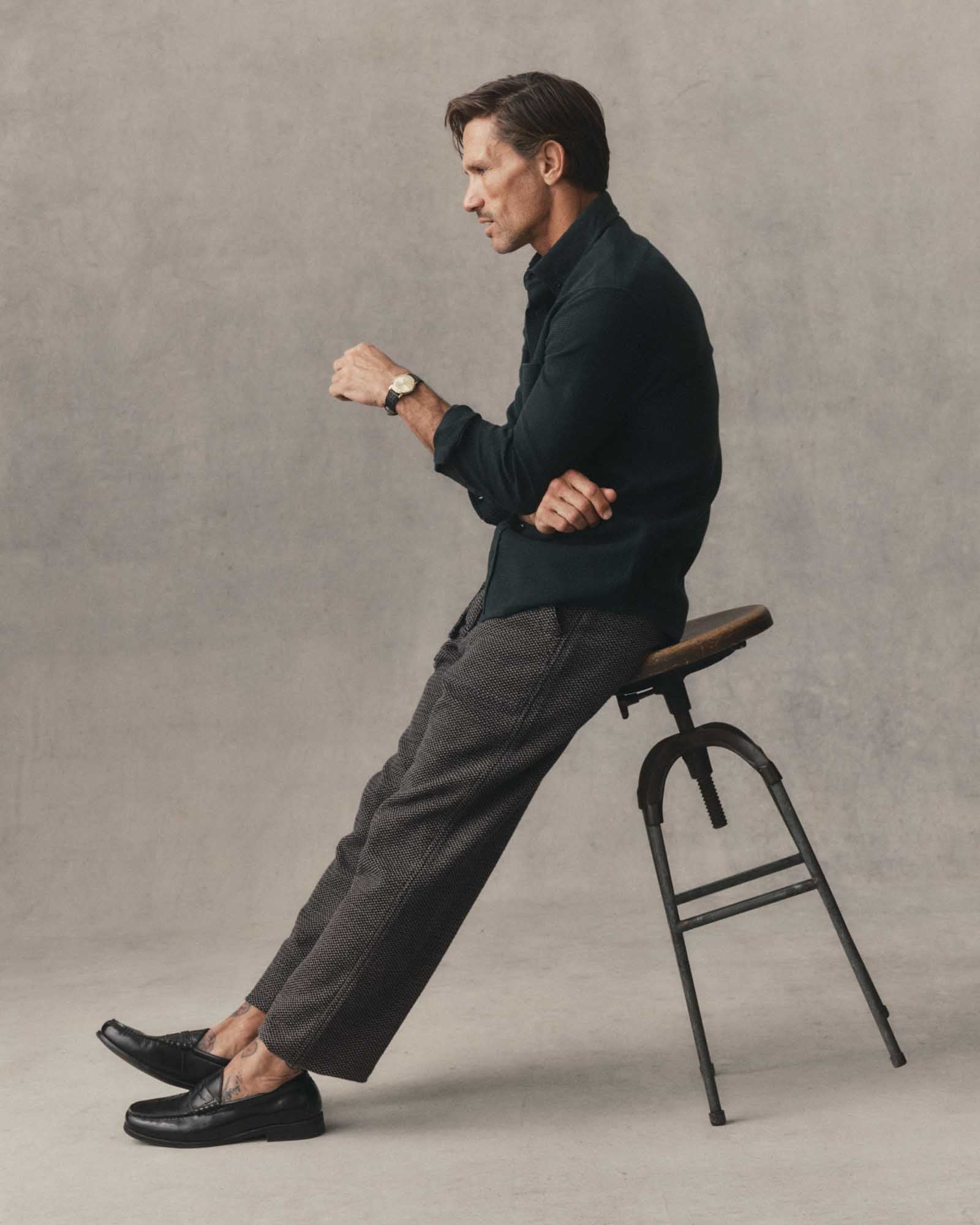 Male model wearing the Taylor Stitch Jack Shirt in Forest Waffle, seated side profile styled with dark trousers and black loafers against a neutral grey background