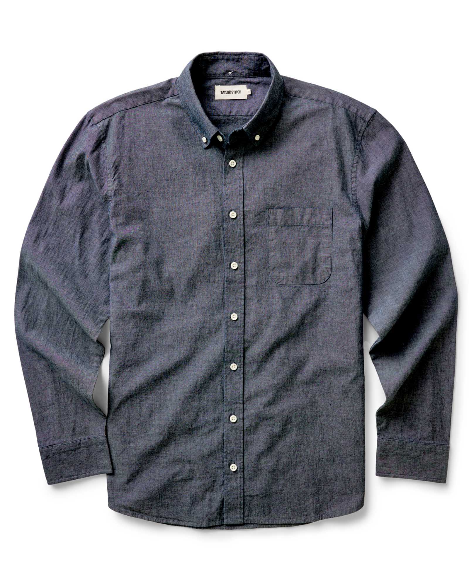 The Jack in Rinsed Indigo Chambray by Taylor Stitch, flat lay front view showing full shirt silhouette, button-down collar, chest pocket, and Taylor Stitch label on a white background