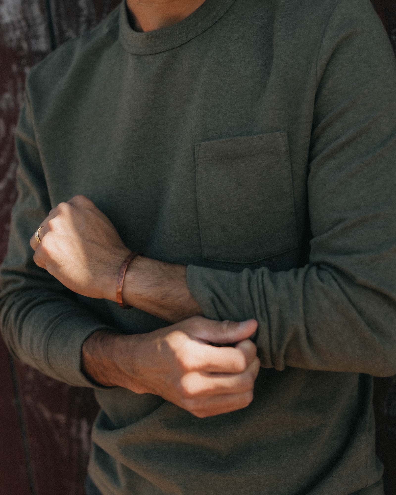 Close-up torso shot of a man wearing The Long Sleeve Shop Tee in Army Twist by Taylor Stitch, showing the chest pocket and ribbed cuff detail with arms crossed