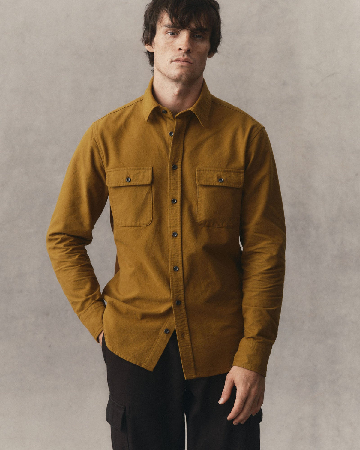 Model wearing the Yosemite Shirt in Saffron untucked with black pants, showing the button front and chest pockets.
