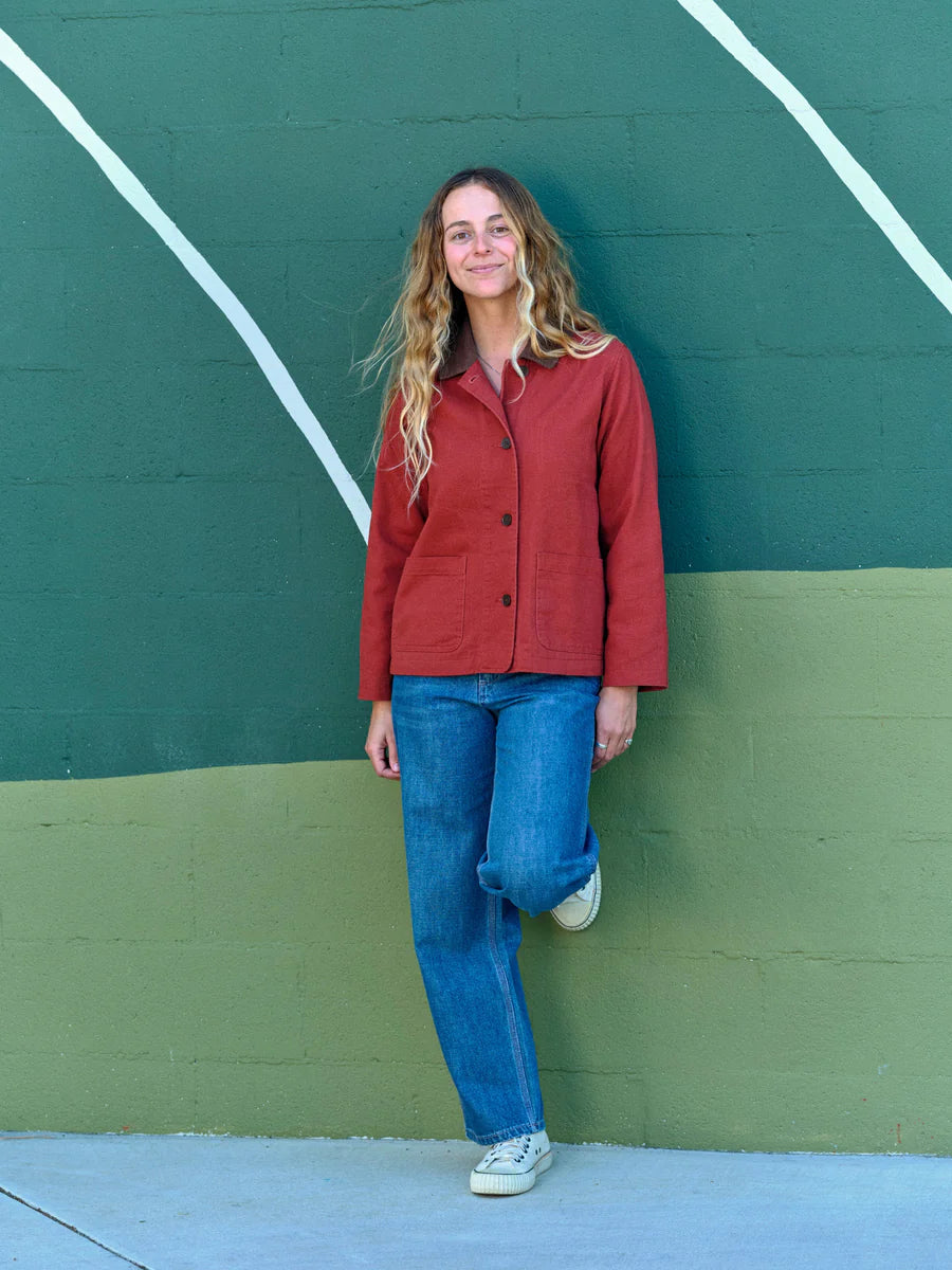 Full-length front view of a woman wearing the Mollusk Lined Painter Jacket in Rust with blue jeans, showing the relaxed boxy silhouette and rust red 100% cotton fabric
