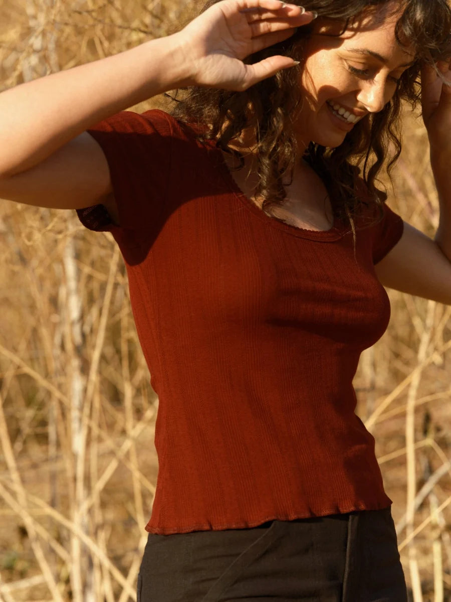 Female model wearing the Mollusk Surf Shop Pointelle Tee in Malbec, three-quarter view showing ruffled hem and fitted pointelle rib fabric in deep malbec red, photographed outdoors in warm natural light