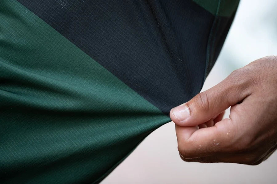 Close-up detail of the Mollusk Surf Shop Stretch Notched Trunks in Black Rover Stripe, showing the stretch nylon fabric being pulled to demonstrate flexibility, with forest green and black colorblock stripe visible