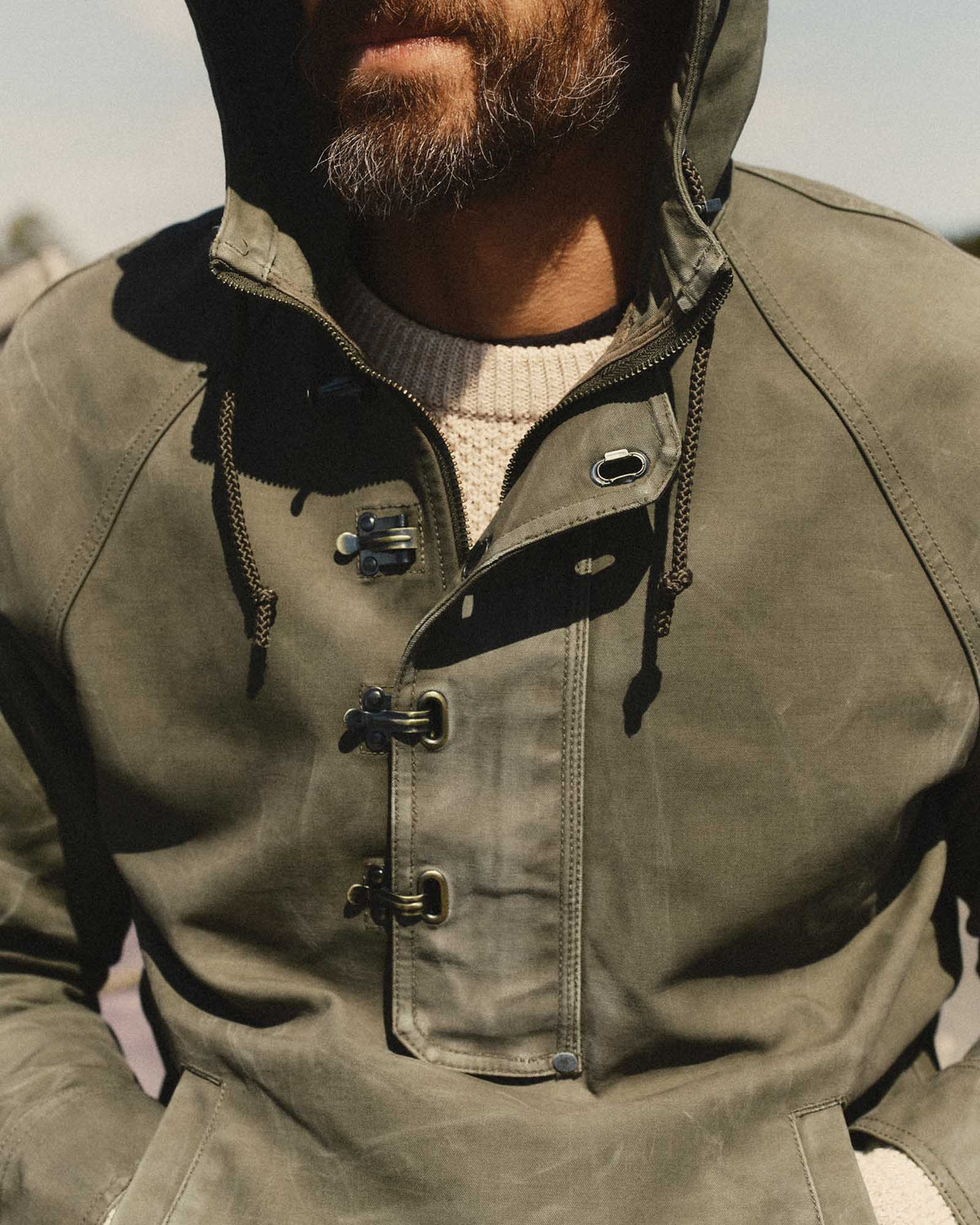Close-up of the Hatteras Anorak’s olive canvas, hood drawcords, zipper, and metal storm-flap clasps.
