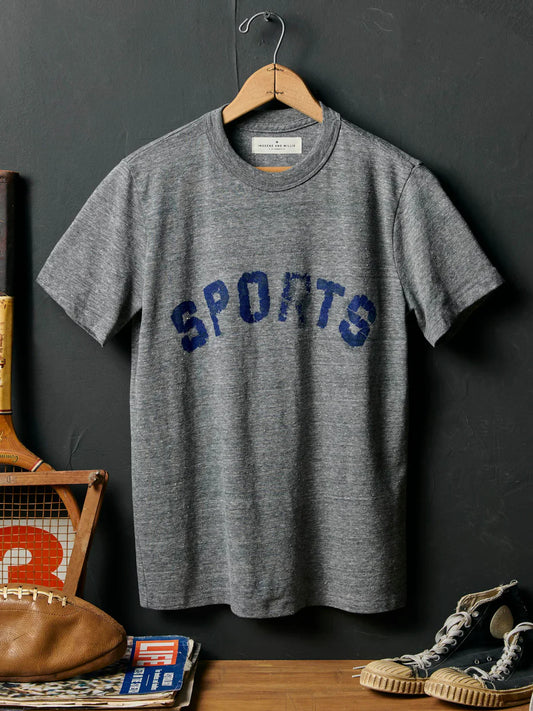 Full front on hanger against dark slate wall, with distressed 'SPORTS' print, styled with football, tennis racket, Life magazine, and sneakers