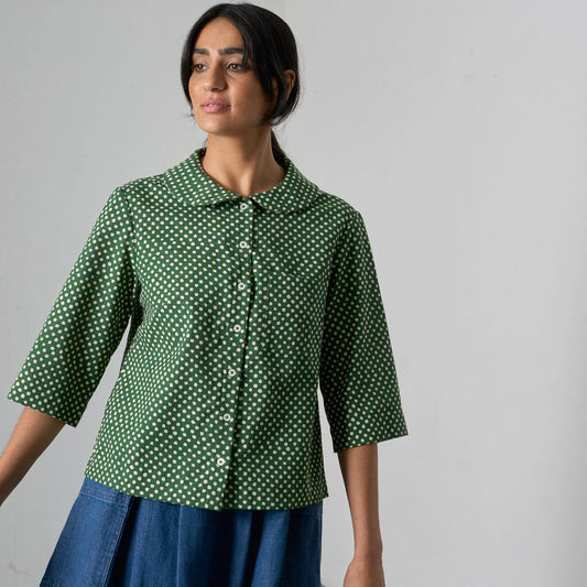 Woman wearing a green polka dot shirt and blue skirt against a gray background