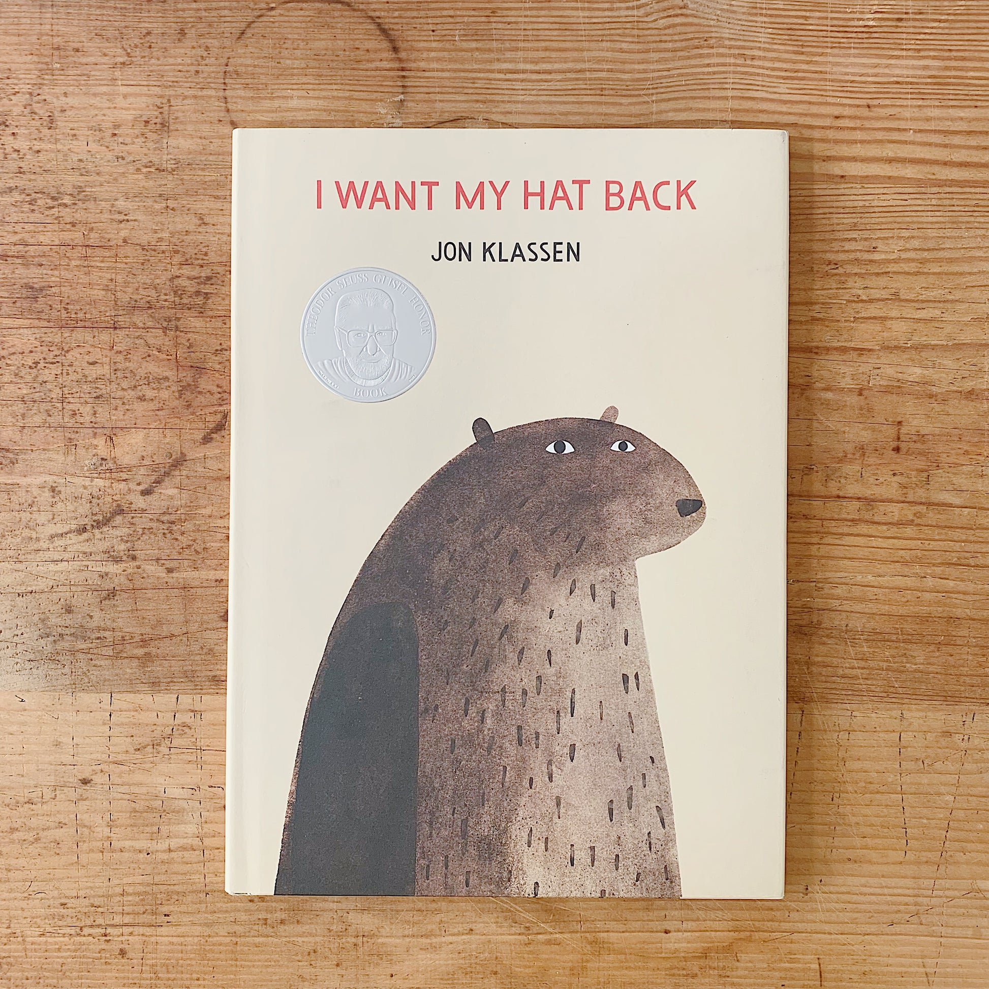 Cover of I Want My Hat Back by Jon Klassen, a cream hardcover featuring a close-up illustration of a large brown bear gazing forward with a Caldecott Honor medal embossed on the upper left
