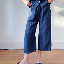 Load image into Gallery viewer, Close up, front view of lower half of model&#39;s legs in navy linen pants and black Birkenstock sandals. Her hands are holding the waistband of the pants. 
