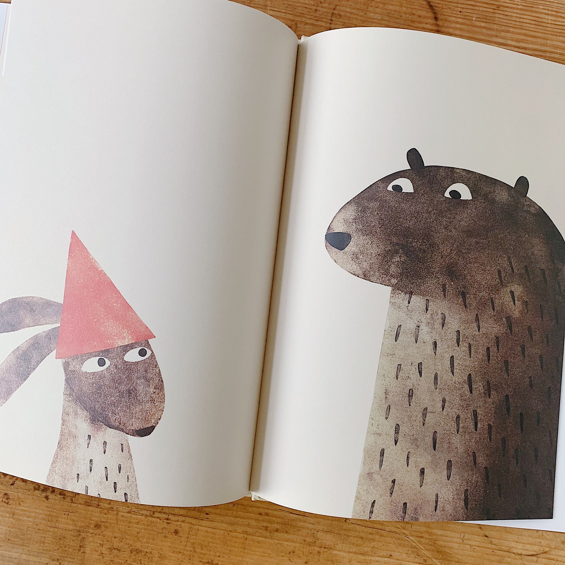 Interior spread of I Want My Hat Back showing a small rabbit wearing a red triangular hat facing the large bear, who stares at the hat with wide eyes, in a wordless confrontational scene
