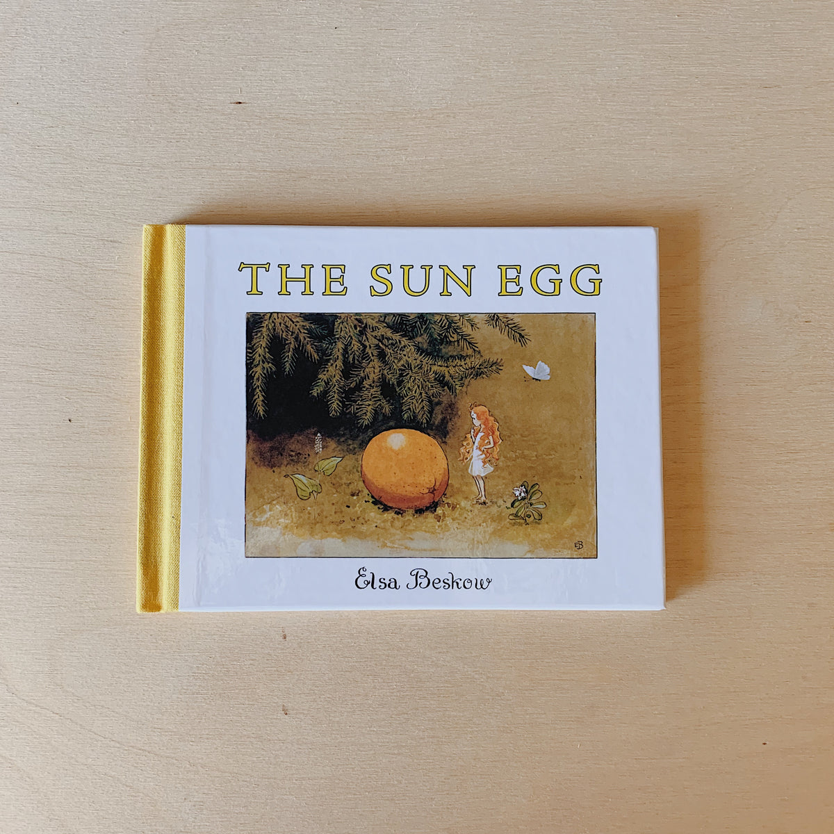 Front cover of The Sun Egg by Elsa Beskow, mini hardcover with a yellow spine, showing a little elf beside a large orange beneath evergreen branches.
