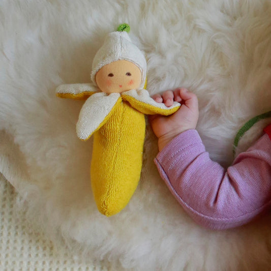 A handmade banana-shaped rattle with a cream cap and yellow terry blanket, held by a baby.
