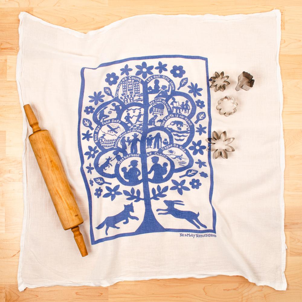 Photograph of a dishtowel printed with a blue tree, people and animals and the words, 