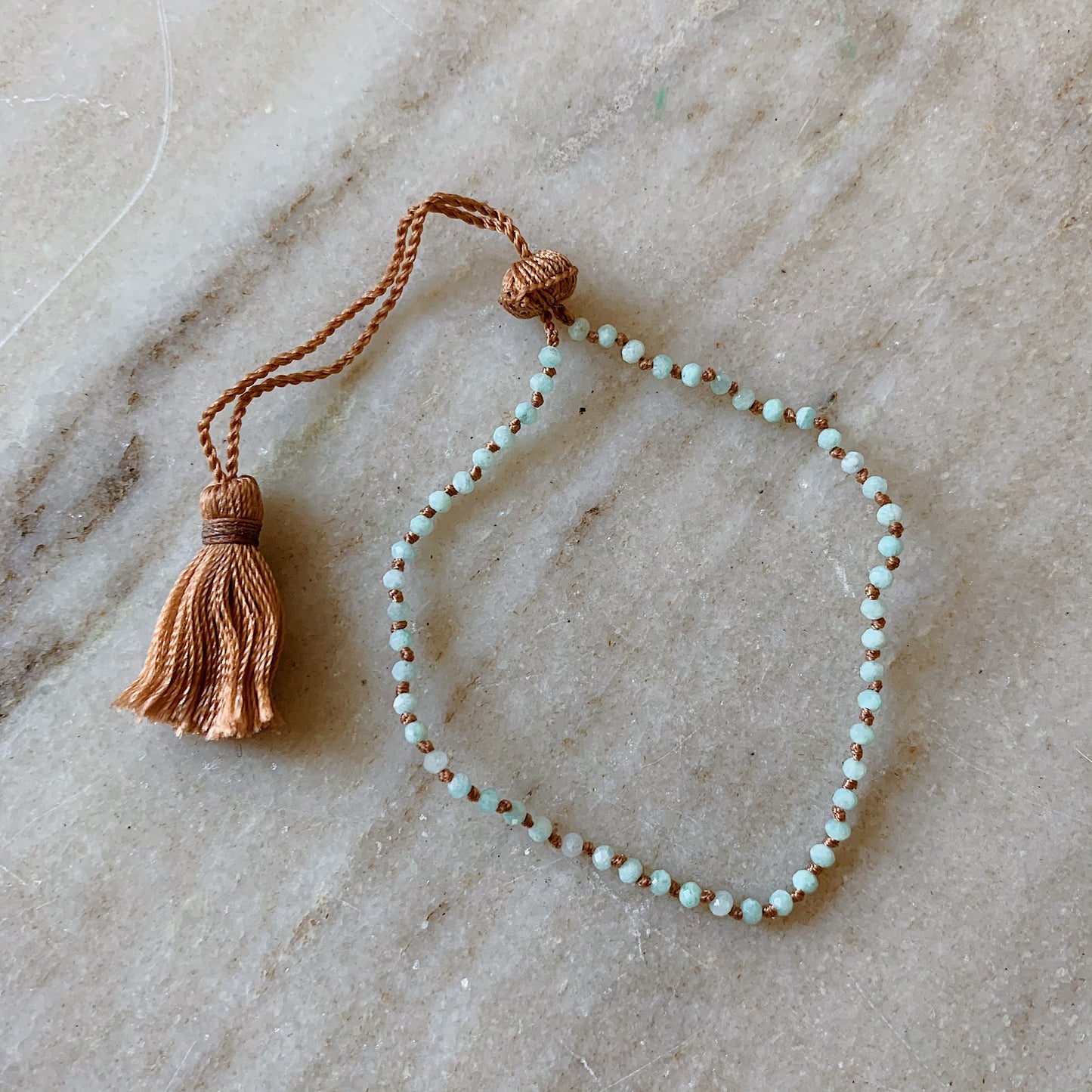Close up overhead shot of Lena Skadegard's tiny amazonite tassel bracelet lying flat on a marble surface