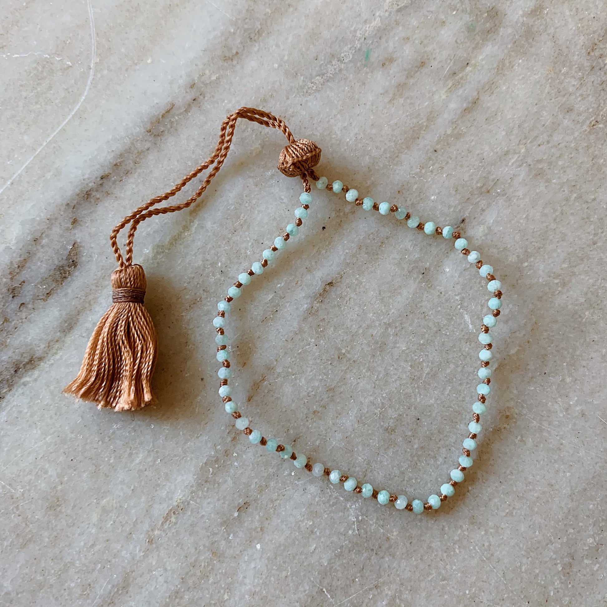 Close up overhead shot of Lena Skadegard's tiny amazonite tassel bracelet lying flat on a marble surface
