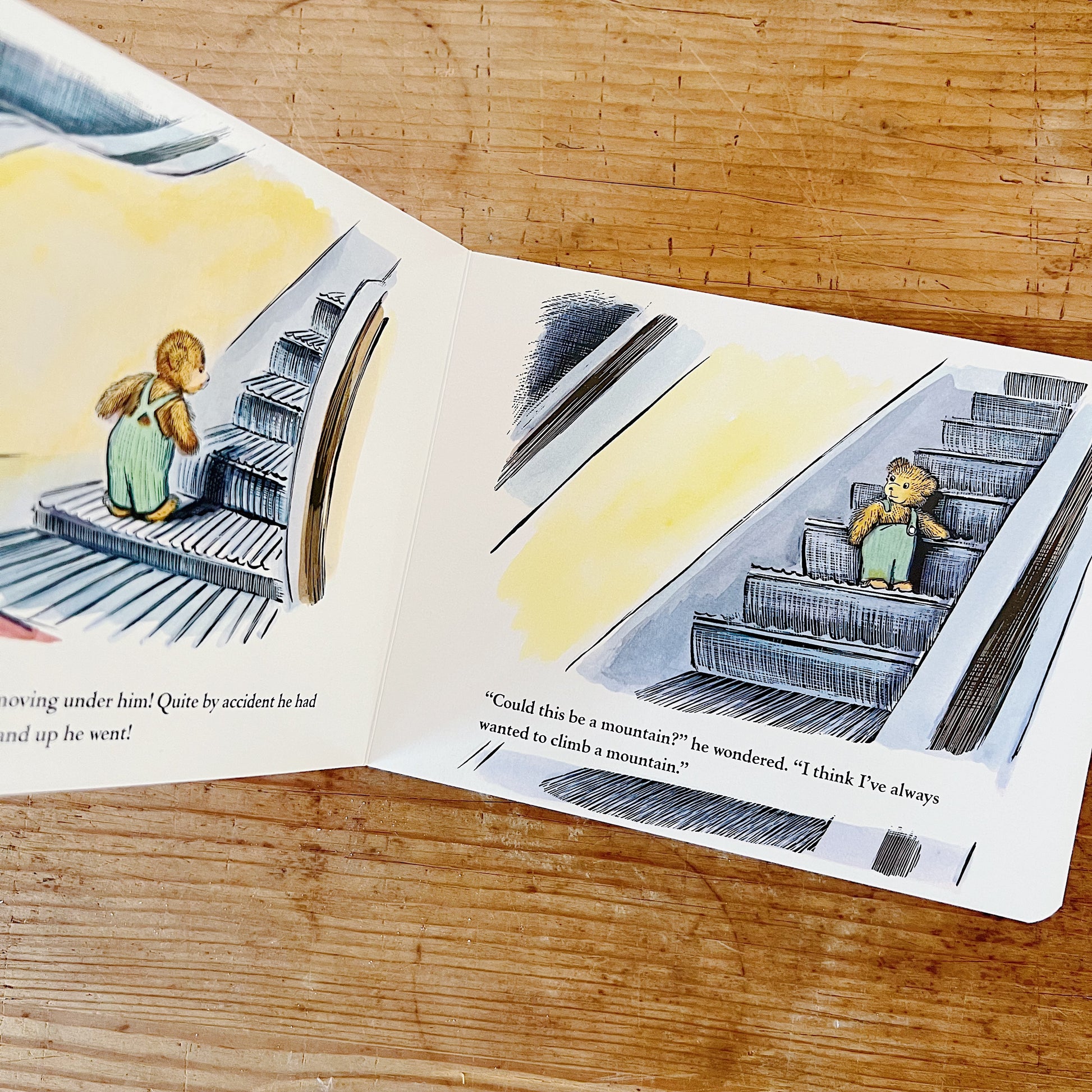 Open interior spread of Corduroy board book showing the escalator scene: on the left page, a partial illustration of Corduroy — a small brown teddy bear in green overalls — riding upward on a moving escalator, with partial text reading "noving under him! Quite by accident he had" and "nd up he went!"; on the right page, a full illustration of Corduroy seated on an escalator step, riding upward past a yellow-lit background, with the text "'Could this be a mountain?' he wondered. 'I think I've always wanted t