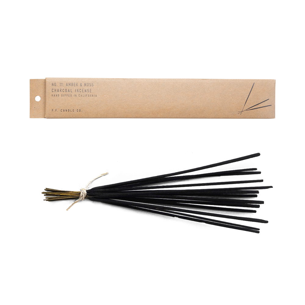 Amber and moss incense lying flat next to its kraft package.