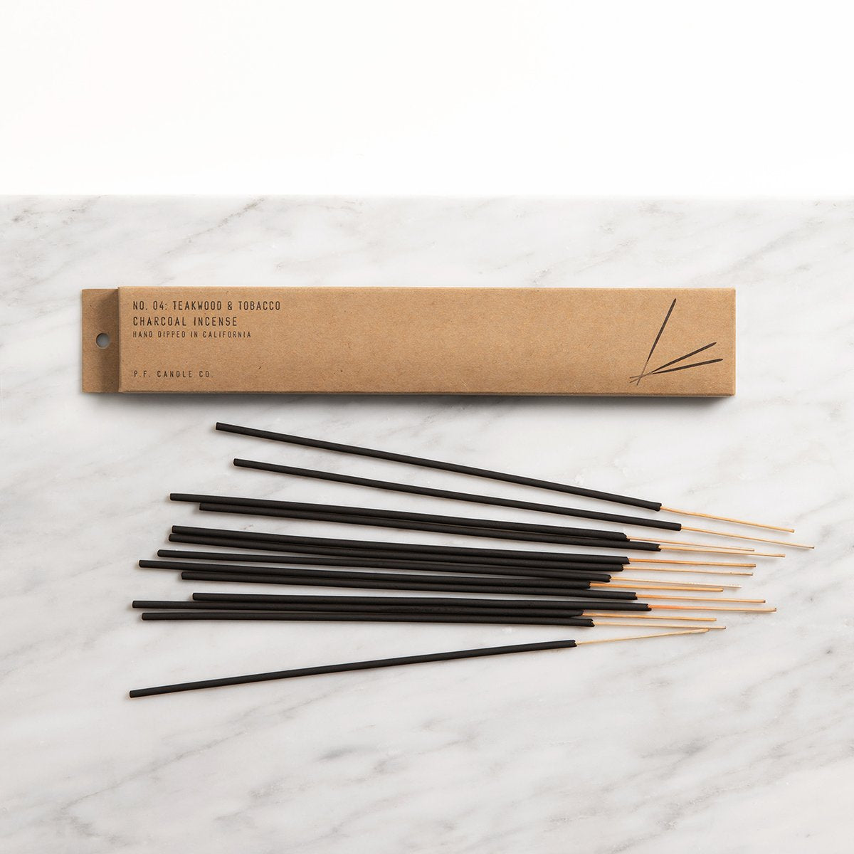 Teakwood and tobacco incense lying next to its kraft package.