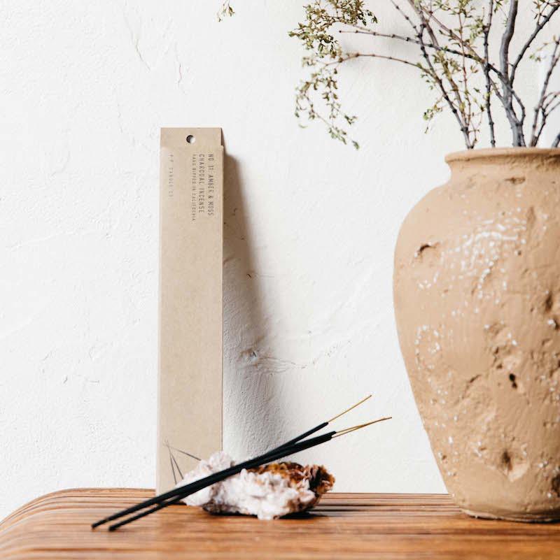 Amber and moss incense resting on a gemstone next to a ceramic vase.