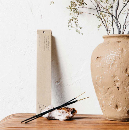 Amber and moss incense resting on a gemstone next to a ceramic vase.