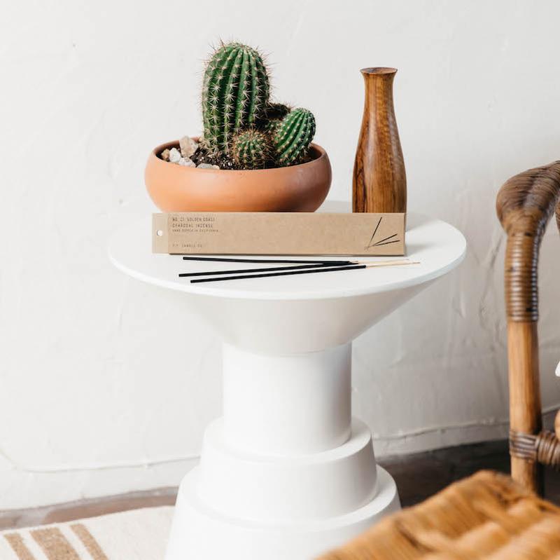 Golden coast incense resting on a small table next to a potted cactus.