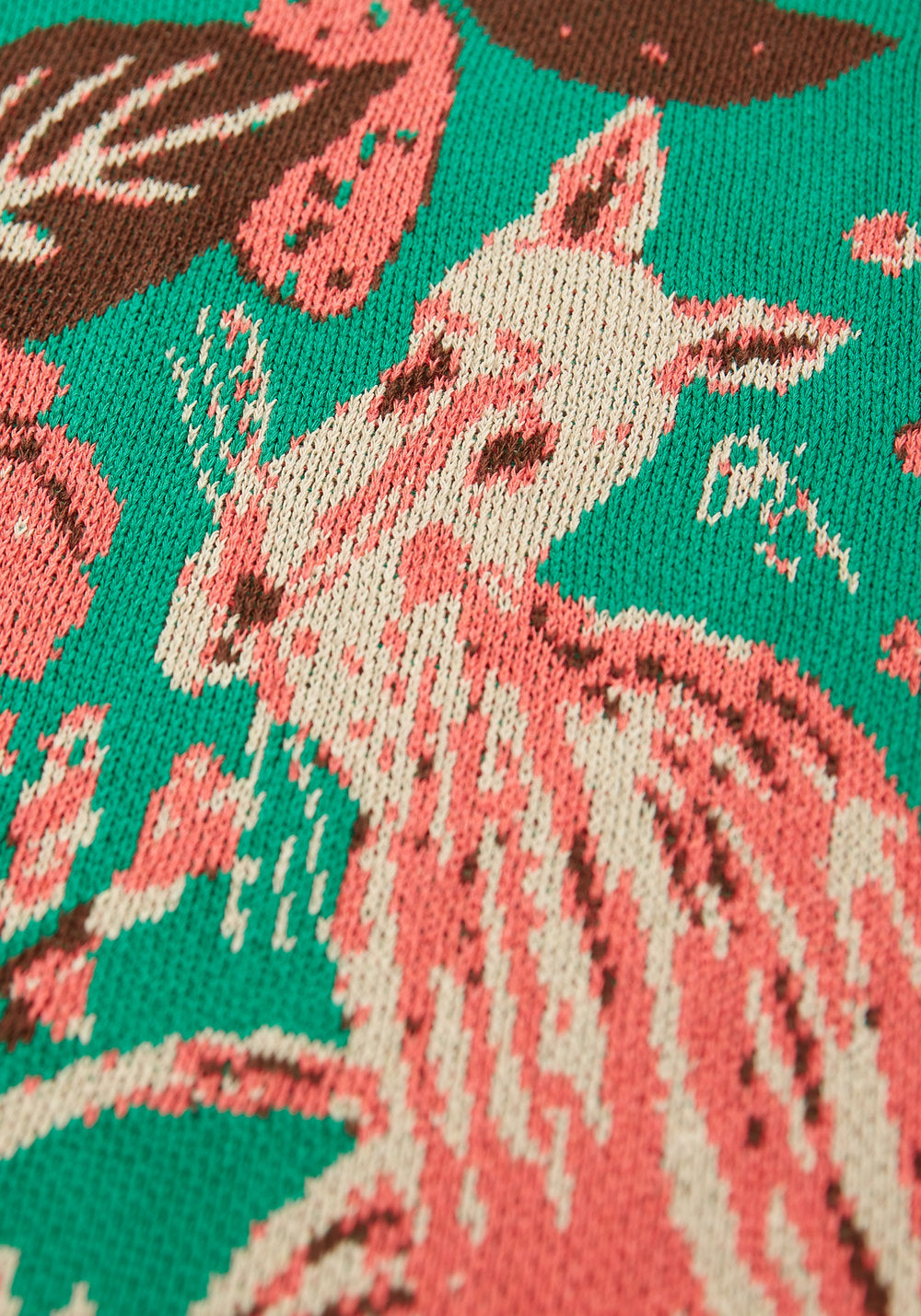 Close-up of a pink and cream woodland animal and brown leaves in the Mushroom Emerald blanket’s green knit.
