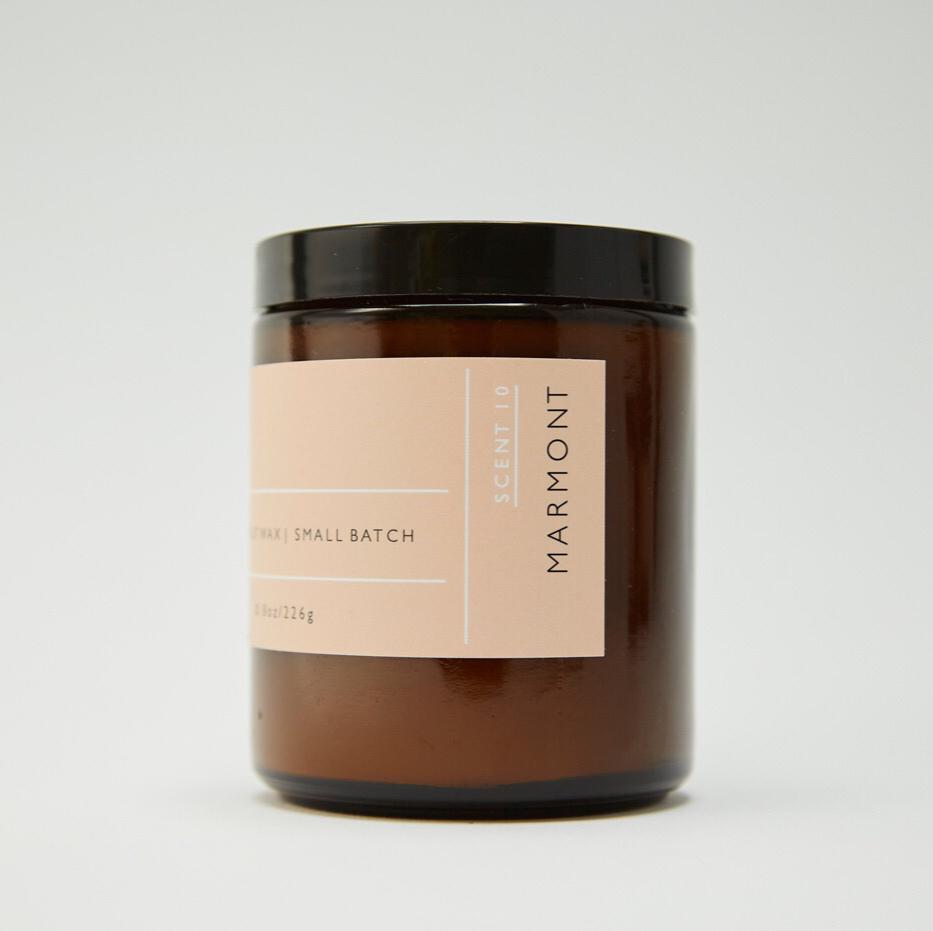 Side view of Roen's Marmont scented candle in an amber brown glass jar with a black lid and pink label.